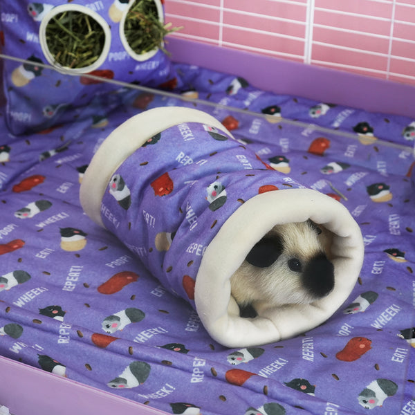 White and black guinea pig in purple fleece tunnel in purple with poop design by brand Kavee. On Purple poop fleece liner in white cage with haybag and pink coroplast in background